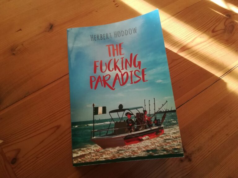 Buchcover The Fucking Paradise liegt auf Holztisch