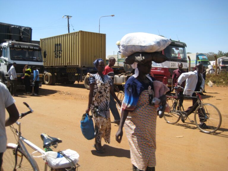 LKW und Menschen in Westkenia, Männer schieben Fahrräder, Frauen in gewickelten Tüchern tragen Säcke